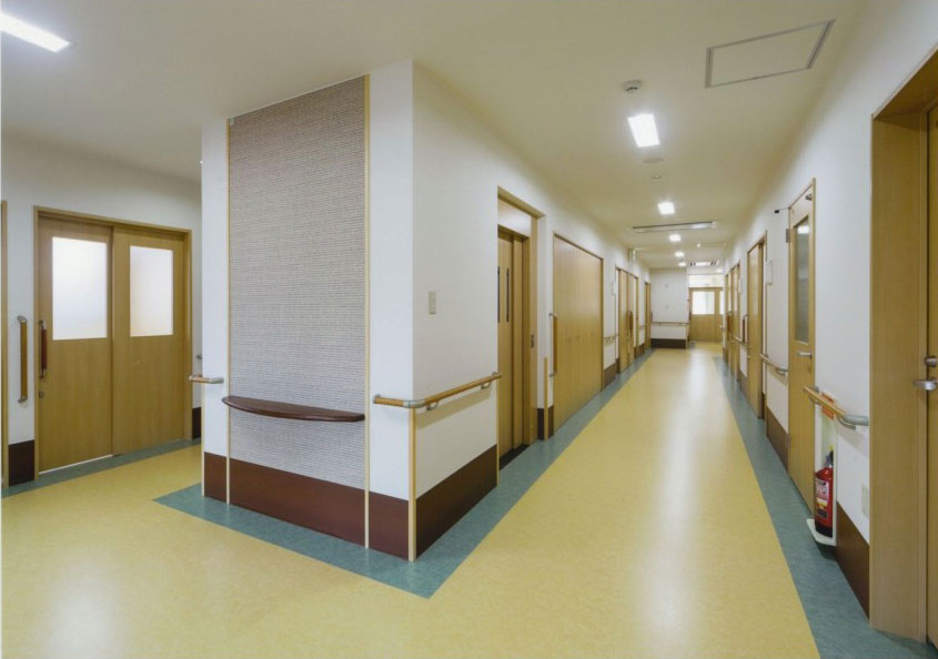 介護施設の廊下。複数の居室ドアと安全柵を備えた広い共用通路。